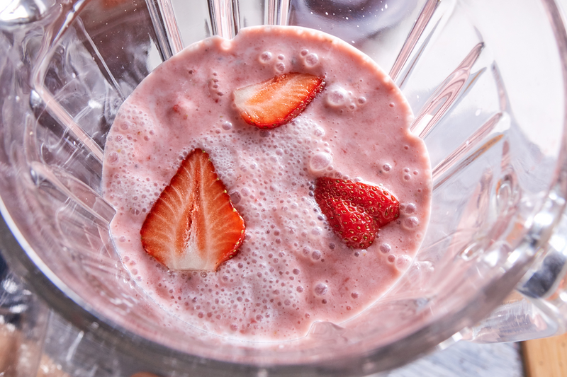 Sicht in einen offenen Standmixer, in dem ein Strawberry Milchshake mit frischen Erdbeeren zubereitet wird