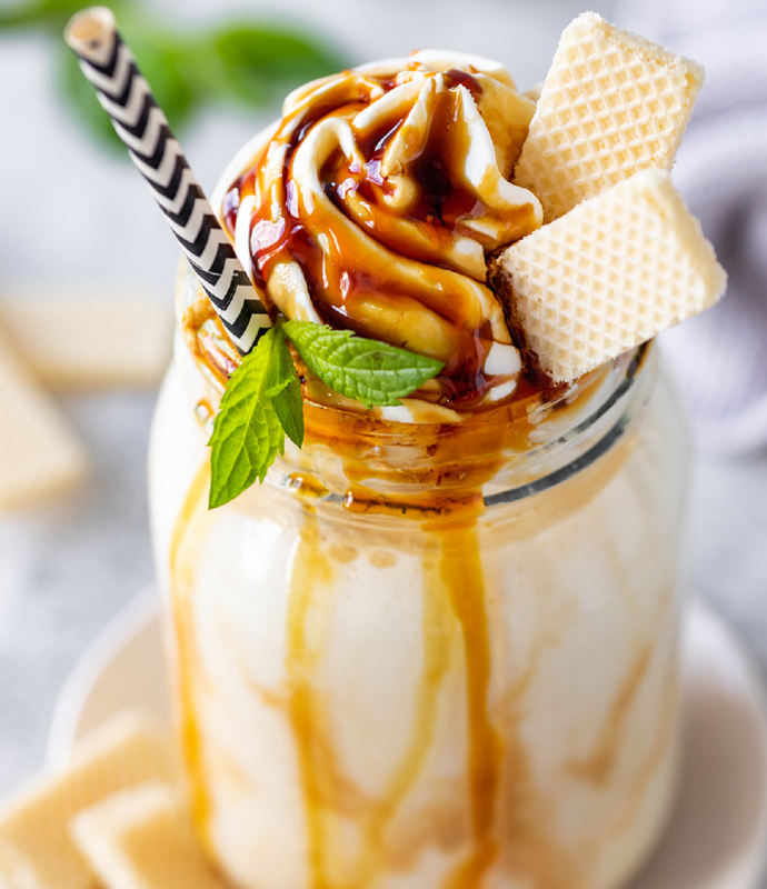 Nahaufnahme eines Vanilla Milchshakes mit Karamellsauce, Keksen und Strohhalm