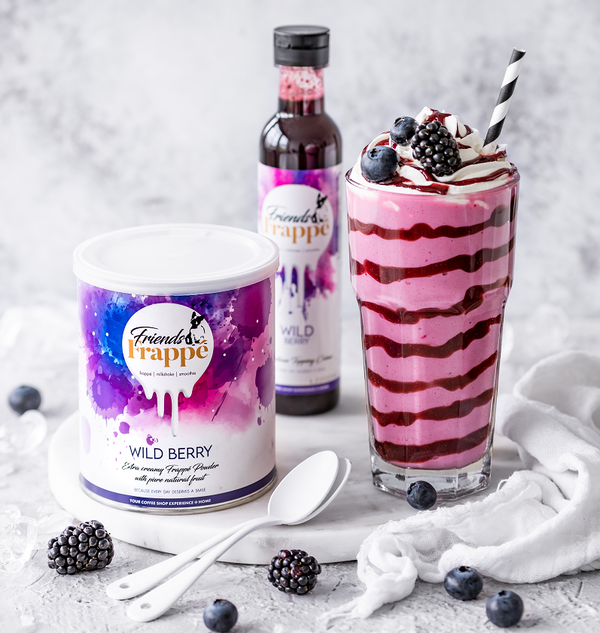 Komposition aus Wild Berry Mix Pulver und Topping Créme neben einem Wild Berry Milchshake