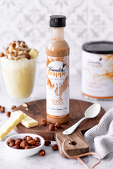 Topping Creme Choc Hazelnut wird neben Haselnüssen, einer weissen Hot Chocolate und der Packung präsentiert