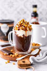 Friends Frappé Hot Chocolate Salted Caramel, dekorativ angerichtet in einem Glas mit Sahnehaube, Karamell und Karamell Chunks